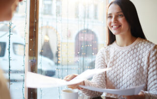 Picture of a teen handing her resume to her interviewer in a cafe for a college admissions interview