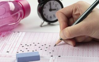 stuudent filling out answer sheet for an exam, with a clock in the background